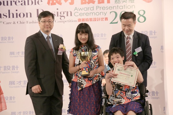 禾輋工場學員鄧惠燕（前排右）擔任康麗時裝設計比賽模特兒，並與設計者（中）及頒獎嘉賓協會副行政總裁李君亮先生（左）在台上合照。 